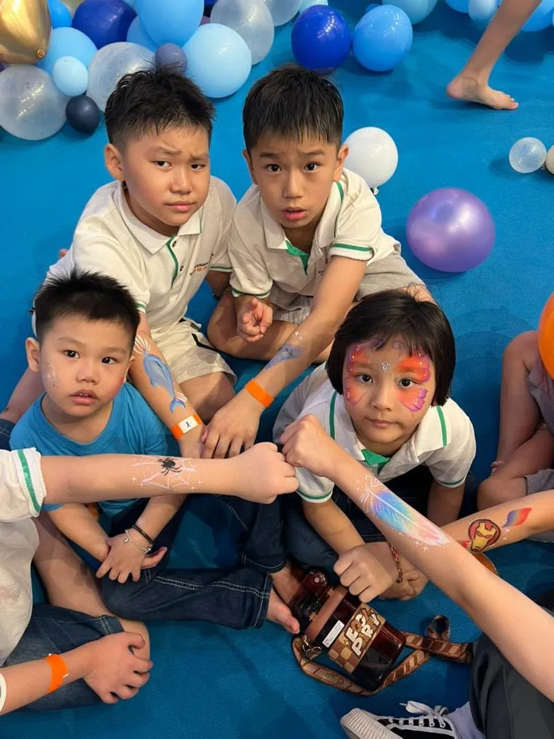 Children with festive face paint and balloon decorations, fist-bumping together on a play mat