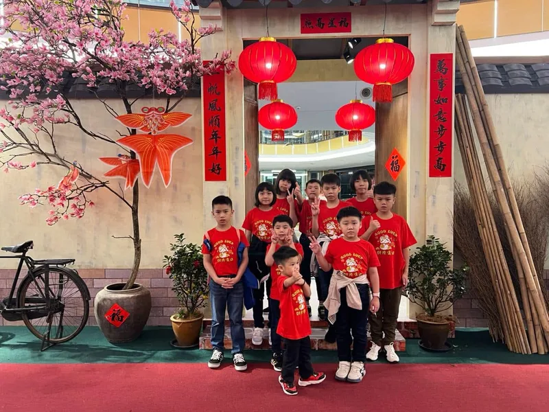 A group of children in matching red 'Good Luck' T-shirts posing together at a shopping mall's Chinese New Year display